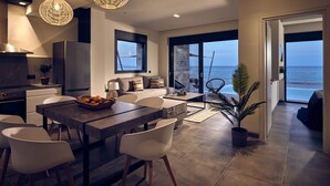 A modern kitchen with a built-in oven, a dining area with a wooden table and white chairs, and a large window overlooking the sea. - Sea Front LaMer Villa,Luxury Retreat & Heated Pool (Zakynthos)