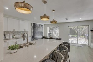 Une cuisine moderne dotée d’un grand îlot central, de luminaires suspendus et offrant une vue sur l’extérieur.