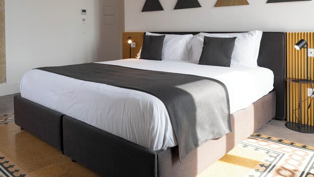 A modern hotel room with a large bed, geometric wall art, a patterned floor, and a wooden headboard. - Ciao Bellini (Naples)