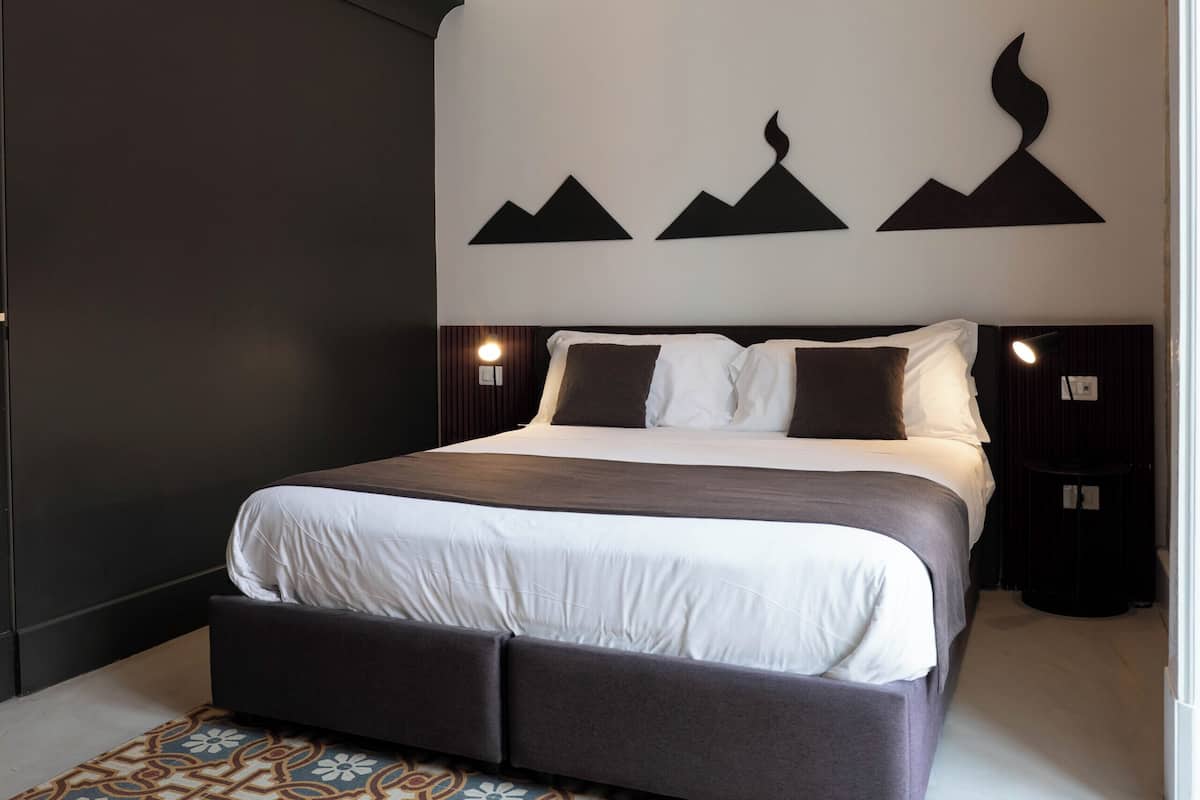 A bedroom with a bed, dark walls, and a patterned rug.