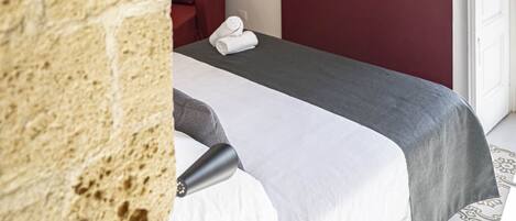 Habitació d'hotel amb paret de pedra, un llit amb mantell blanc i gris, una cadira vermella i un televisor de pantalla plana muntat a la paret.