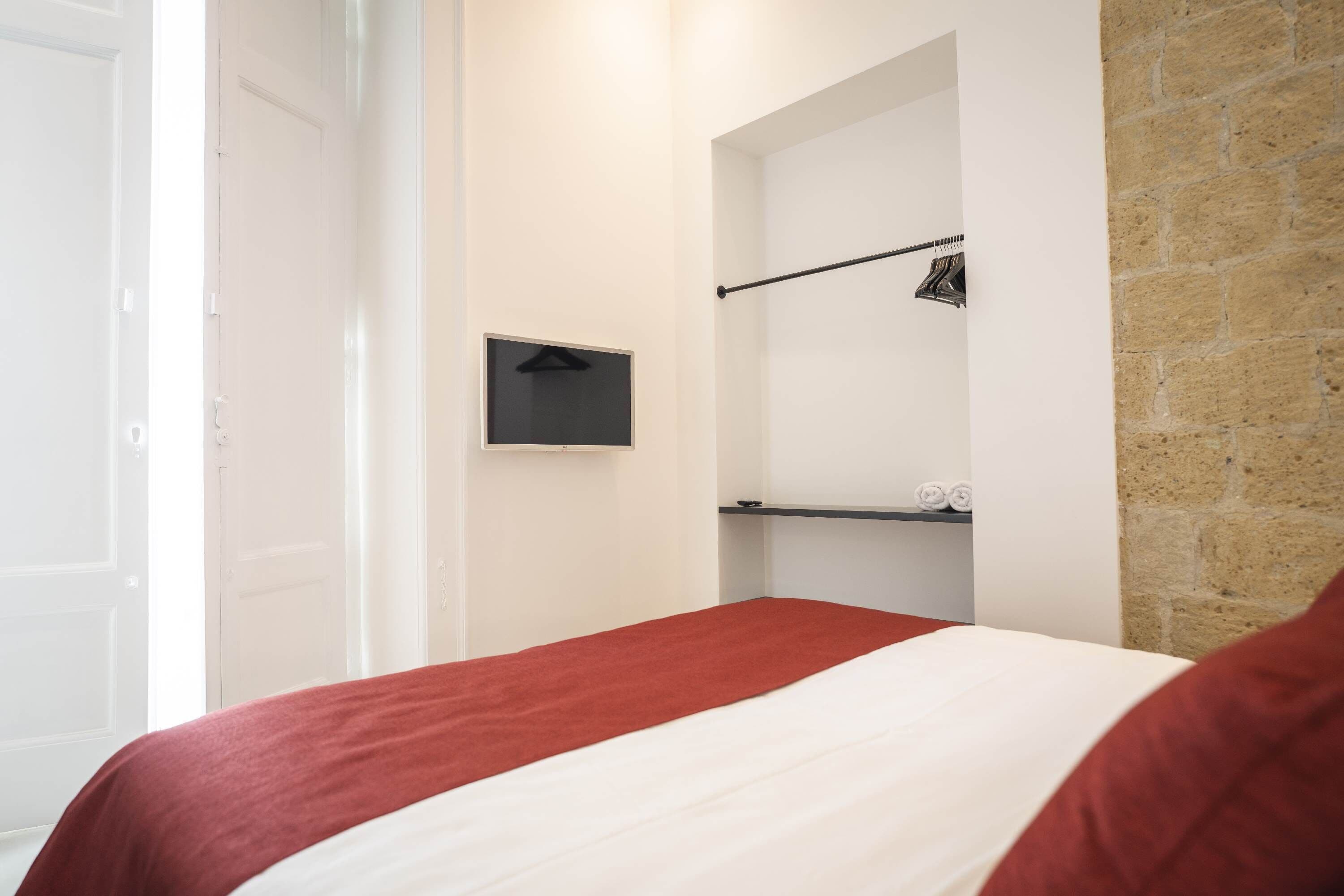 Et hotelværelse med en seng, et knagered og en hylde med håndklæder.