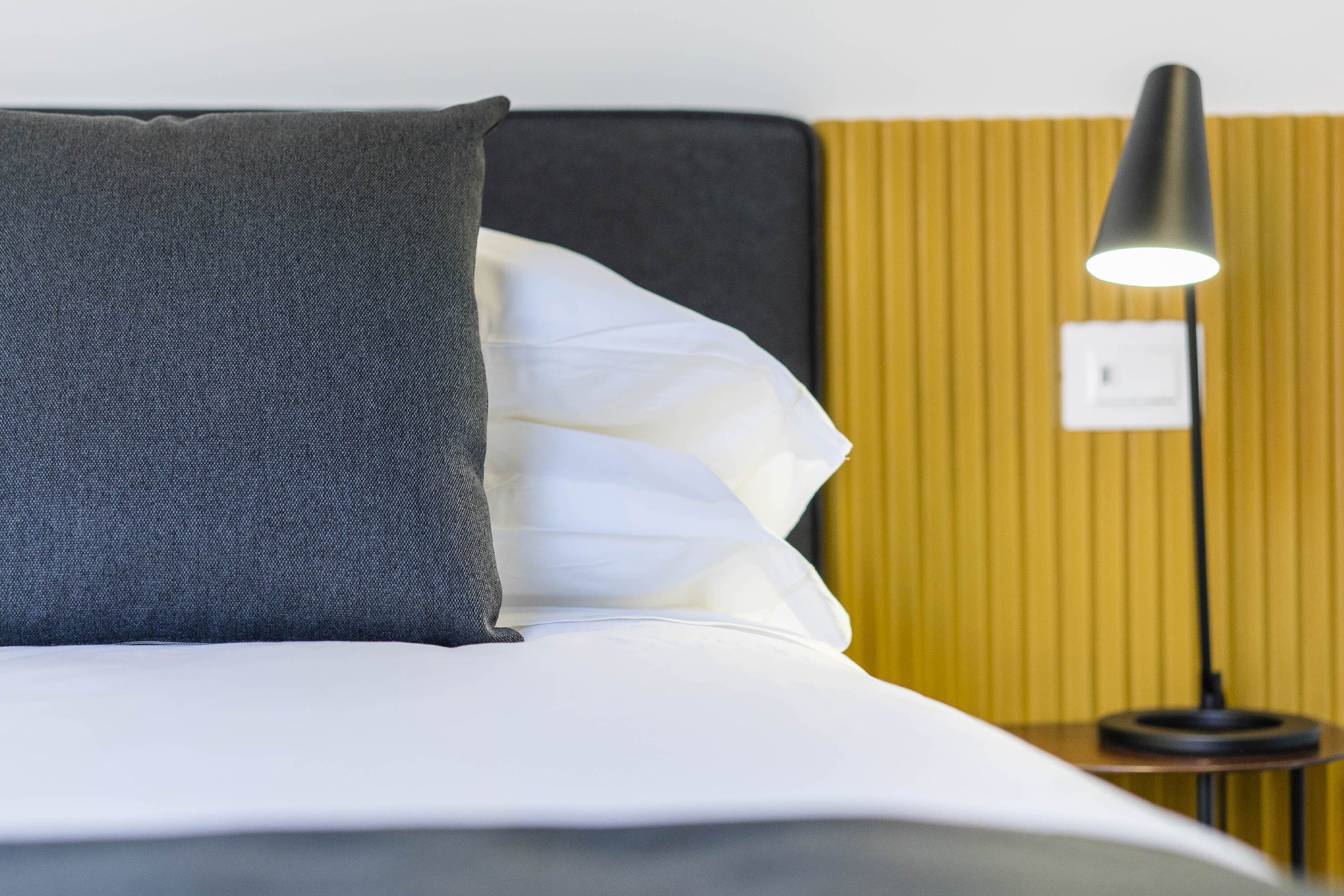 A neatly made bed with white and grey bedding, a black headboard, and a bedside lamp.