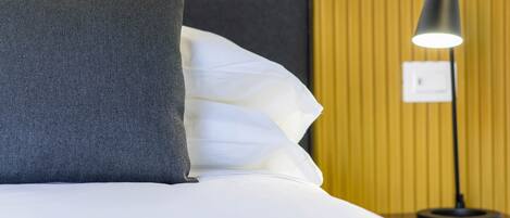 A neatly made bed with white and grey bedding, a black headboard, and a bedside lamp.