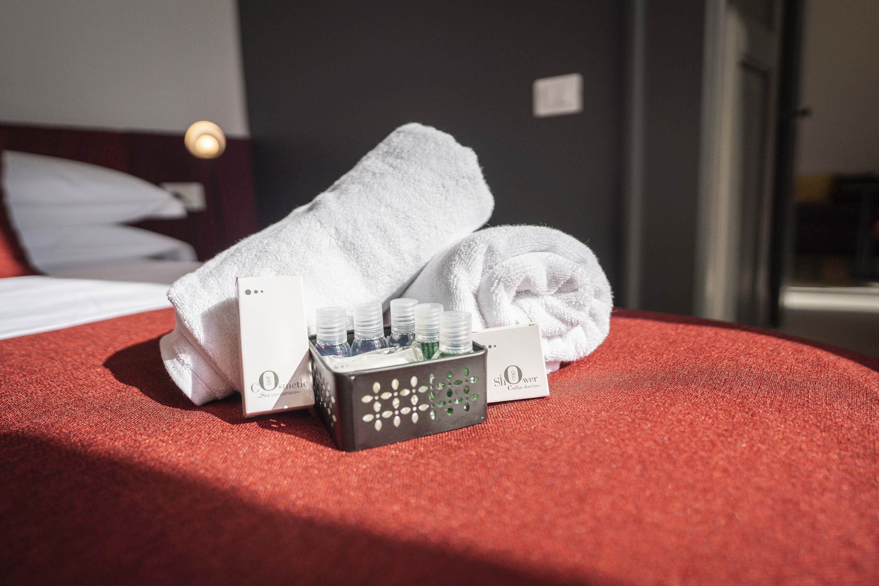A neatly made bed with white towels, a bottle of Olay cleanser, and a bottle of Olay cleanser in a black box.