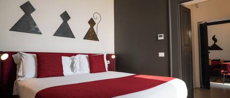 A hotel room with a large bed, red and white bedding, a modern wall art piece, and a view into the adjacent room.