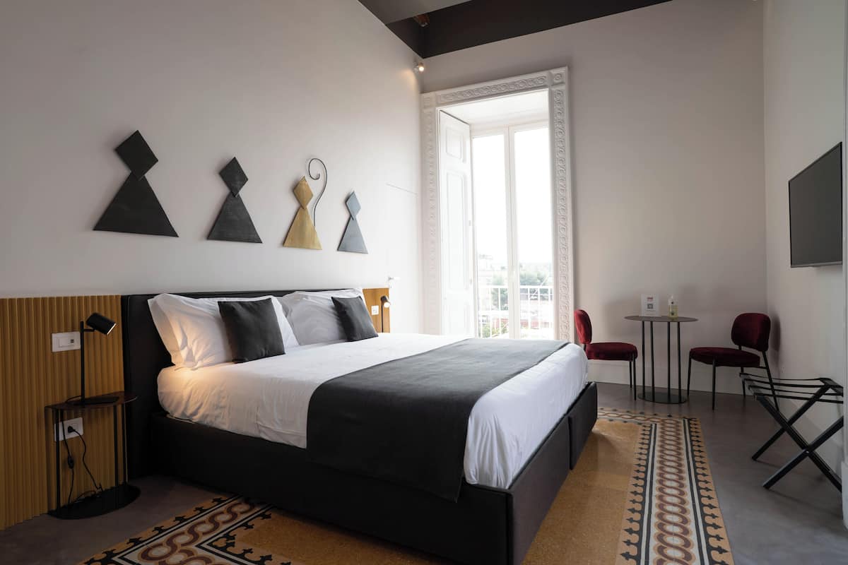 A modern hotel room with a large bed, a small table, two chairs, and geometric wall art.