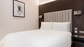 Ein Hotelzimmer mit einem großen Bett, einer Kopfteilbeleuchtung, einem Nachttisch und einer Wandlampe.