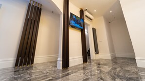 Un moderno vestíbulo de hotel con suelo de mármol, un televisor de pantalla plana en la pared y un panel decorativo de madera.