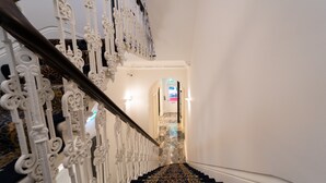 Una escalera con barandales blancos ornamentados y alfombra estampada que conduce a una puerta con pantalla digital.