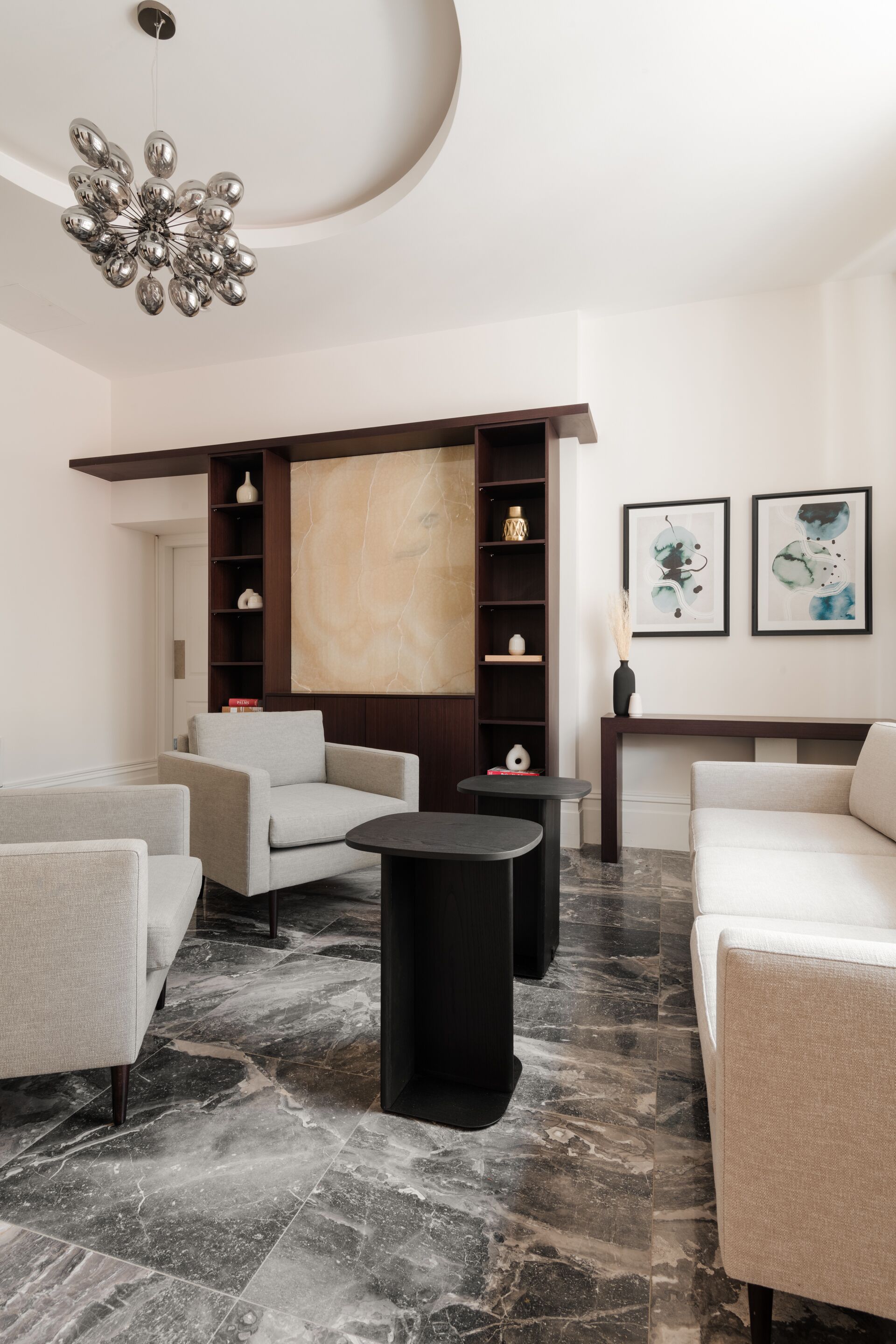 Un salon moderne avec un sol en marbre, un canapé, des fauteuils, une table basse, une bibliothèque et un grand tableau abstrait accroché au mur.