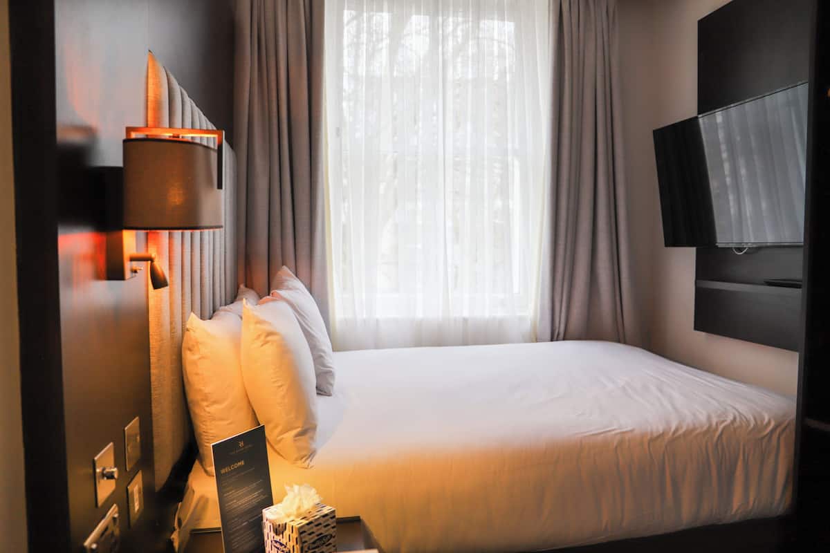 A hotel room with a bed, curtains, a wall-mounted TV, and a welcome sign.