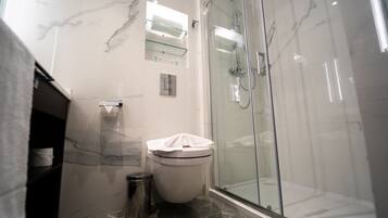 A modern bathroom with a glass-enclosed shower, a marble-tiled wall, and a toilet with a paper towel holder.