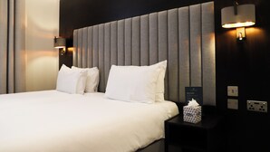 Habitación de hotel con una cama grande, dos lámparas de noche, una mesita de noche con una caja de pañuelos y un cartel en la pared.