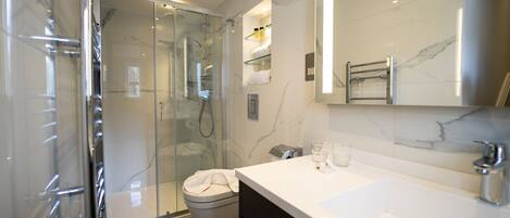 A modern bathroom with a glass-enclosed shower, a white sink, and a marble-tiled wall.