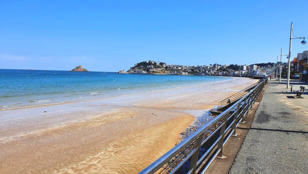 A coastal promenade with a sandy beach, a metal railing, and a clear view of the sea and distant hills. - SEAFRONT APARTMENT VAL ANDRE ALL INCLUSIVE FOR 5 PEOPLE (Pléneuf-Val-André)