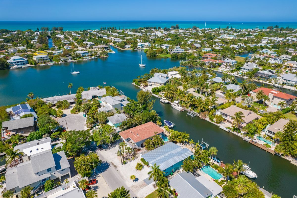 Vue aérienne d’une zone résidentielle côtière, avec des maisons, une marina et un ciel bleu dégagé.