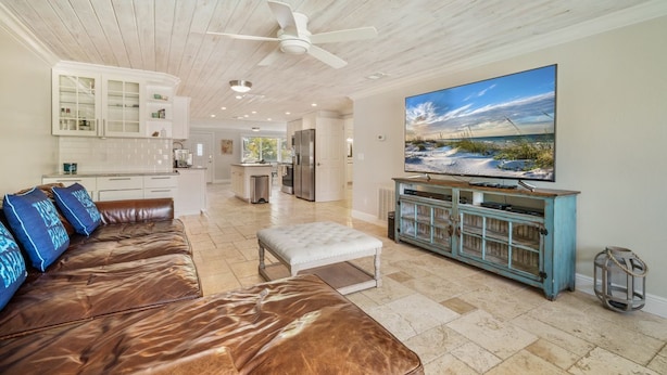 A spacious living room with a leather sofa, a large flat-screen TV, and a wooden ceiling fan.