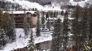 A lodge with multiple floors, surrounded by snow-covered trees and a ski slope in the background. - Newly Remodeled Condo Wren 201 with Creekside Views of Vail Mountain by RedAwning (Vail)