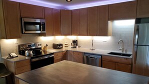 A modern kitchen with wooden cabinets, stainless steel appliances, and a central island. - Newly Remodeled Condo Wren 201 with Creekside Views of Vail Mountain by RedAwning (Vail)