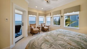 A bedroom with a large bed, two chairs, a ceiling fan, and a view of the ocean through a sliding door. - Bella Vista: Bay front with gorgeous views and outdoor living space. (Anna Maria)