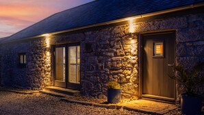 A stone building with two doors and windows, each illuminated by warm lighting. - Rural Barn Conversion (Truro)