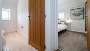 A bedroom with a wooden door, a bed, a nightstand, and a framed picture on the wall. - Rural Barn Conversion (Truro)