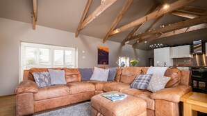 A spacious living area with a leather sectional sofa, a wooden dining table, and a kitchen in the background. - Rural Barn Conversion (Truro)
