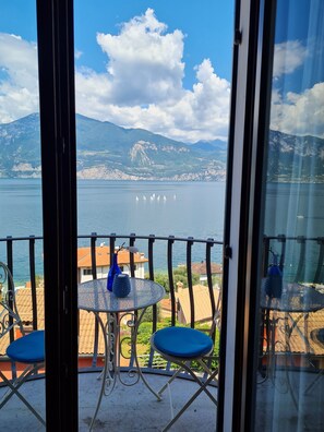 Ein Balkon mit Tisch und Stühlen mit Blick auf einen See, auf dem Segelboote fahren, mit Bergen im Hintergrund.