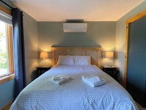 Una cama bien tendida con una colcha estampada, dos lámparas de noche y una ventana con cortinas.