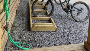 Puinen pyöräteline, jossa on pyörä, puinen penkki ja katettu ulkotila, jossa on tila puille.