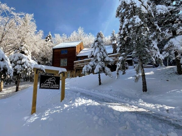 Una cabaña de madera llamada "Cupp's Cabin" rodeada de árboles cubiertos de nieve.