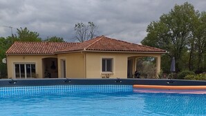Una piscina amb un videtatge de rajola, un edifici amb teulada de rajola i arbres al fons.