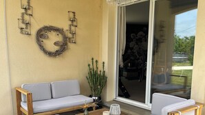 Zona de pati acollidora amb un sofà de fusta, dues cadires blanques amb coixins, una taula de cafè de fusta i un llum penjant.