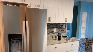 Eine Küche mit Edelstahl-Kühlschrank, weißen Schränken und einer Arbeitsplatte aus Granit, sowie einem Wasserspender.