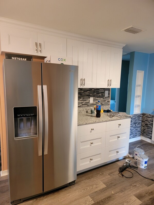 A kitchen with a stainless steel refrigerator, white cabinets, a granite countertop, and a water dispenser.