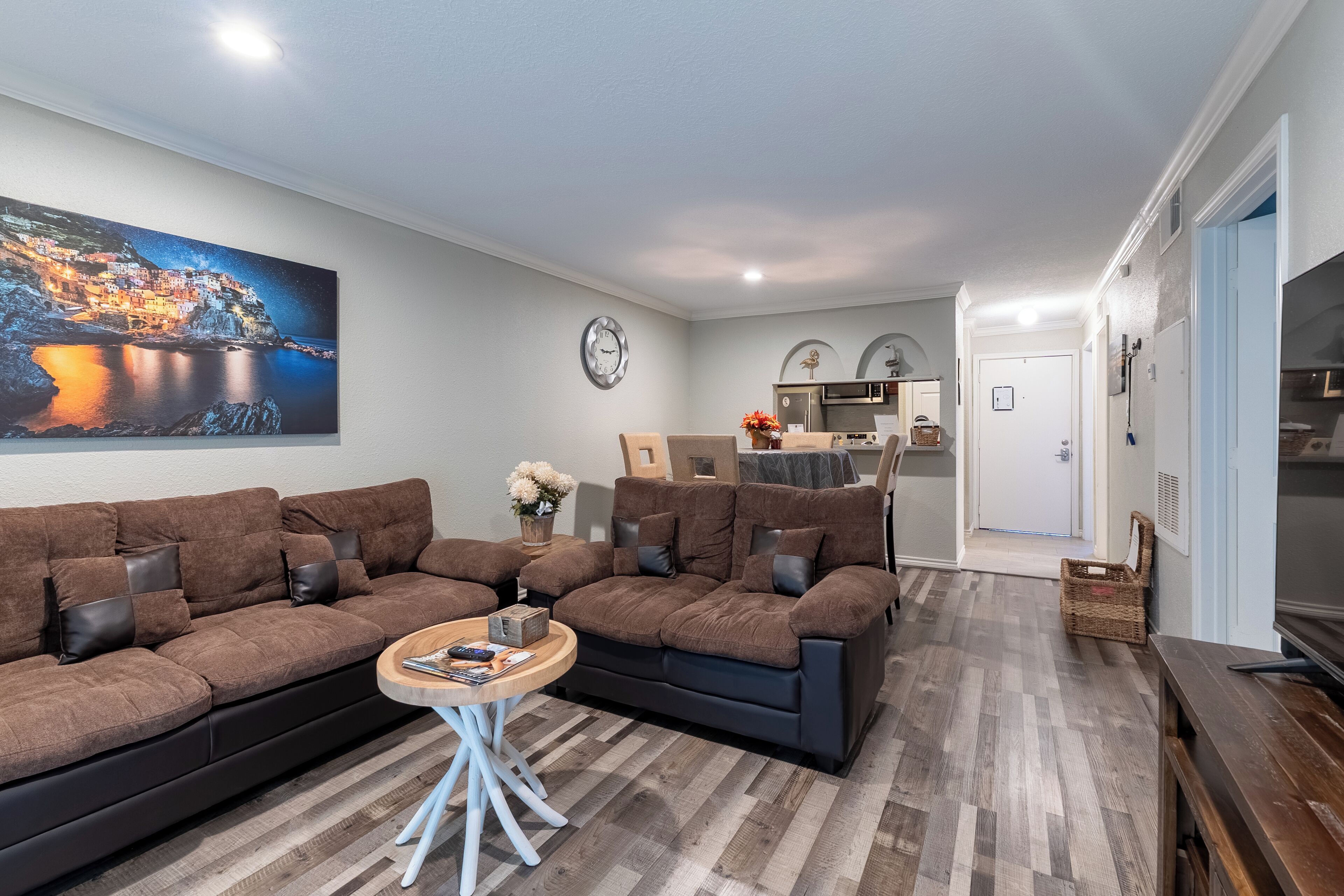 A modern living room with a large brown sectional sofa, a round coffee table, and a cityscape painting on the wall.