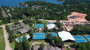 Vista aérea de una zona residencial con varias canchas de tenis, una piscina y una gran masa de agua al fondo.