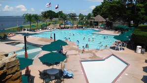 Una piscina con varias pistas, rodeada de tumbonas y sombrillas, con banderas y vistas al mar.