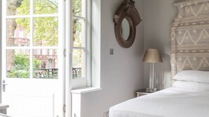 Quarto com uma janela grande, um espelho, abajur e cabeceira estampada.