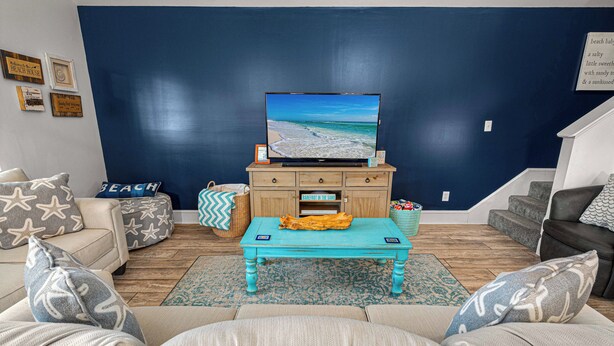 Un soggiorno con una grande TV a schermo piatto, un mobiletto in legno e un tavolino da caffè blu.