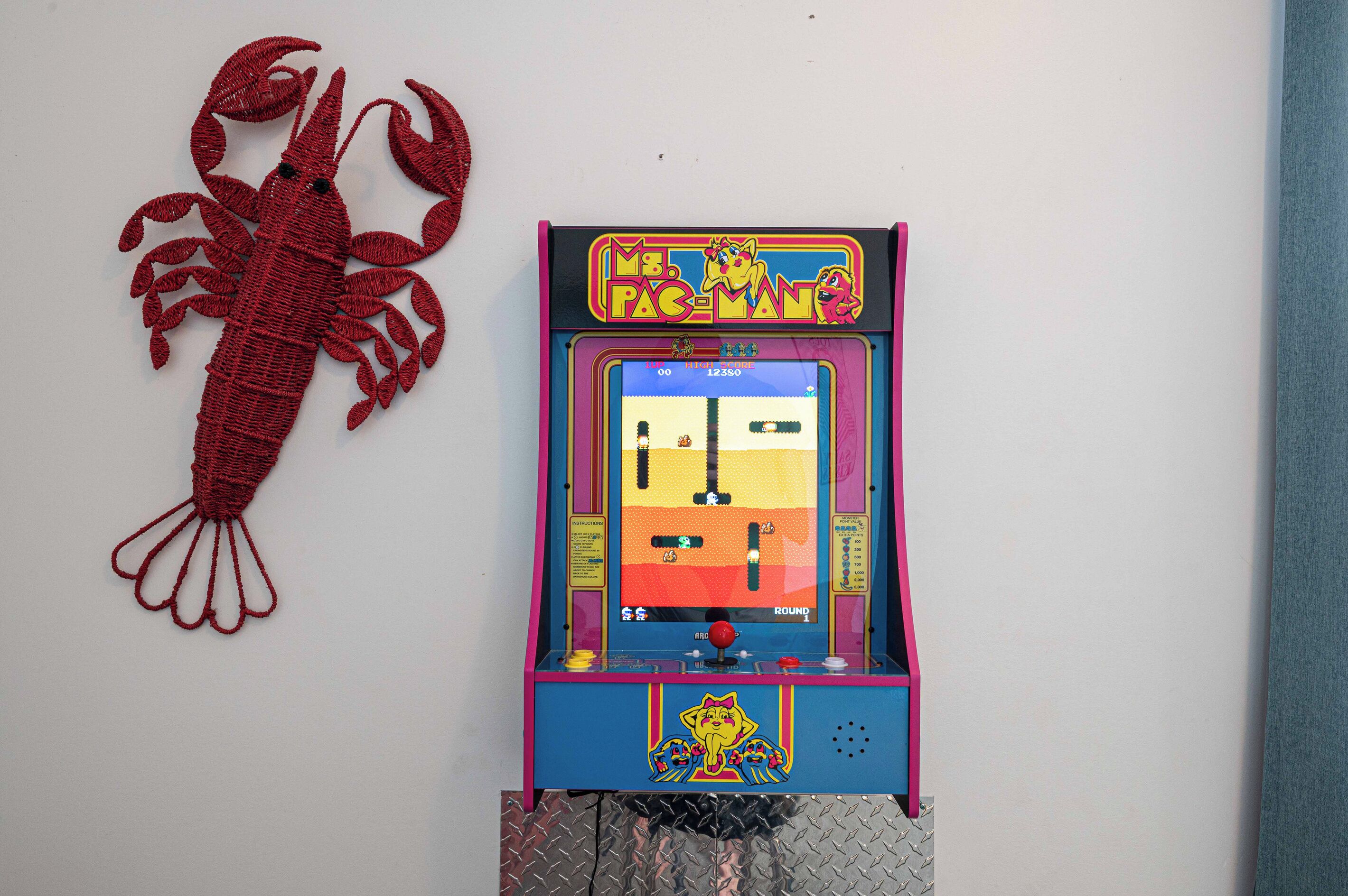 Een claw machine spelautomaat met een high score display en een decoratie van een kreeft aan de muur.