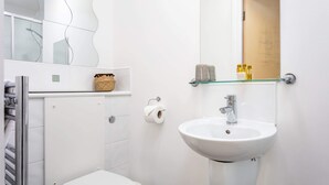 Un bagno moderno con un water bianco, uno scaffale in vetro con articoli da toilette, un lavandino bianco e uno specchio sopra il lavandino.