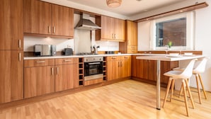 Una cucina moderna con mobili in legno, elettrodomestici in acciaio inossidabile e un'area pranzo con sedie bianche.