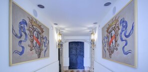 Un pasillo con piso de cuadros, dos cuadros decorativos en las paredes y una puerta azul al final.