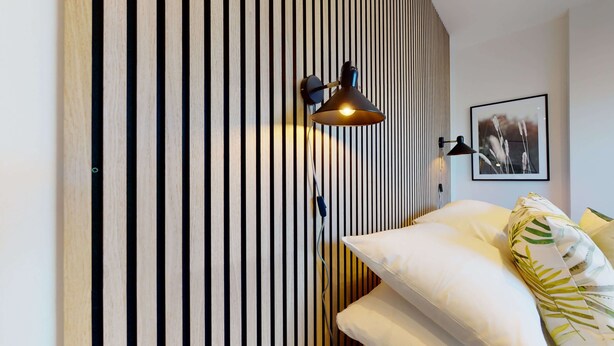 Een slaapkamer met een gestreept behang, een bed met wit beddengoed, een zwarte lamp en een ingelijst schilderij aan de muur.