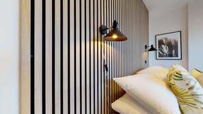 A bedroom with a striped wall, a bed with white bedding, a black lamp, and a framed picture on the wall. - The Oxford Lodge Exeter Room | Oxford Holiday Let | 1 Bed & Sleeps 2 (Oxford)