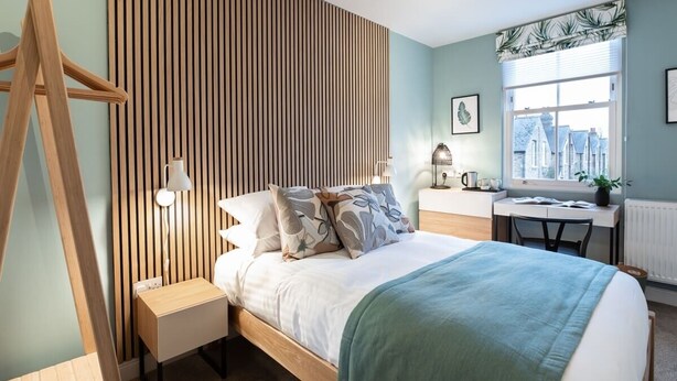 A modern bedroom with a bed, bedside table, lamp, and a view of the city through a window.