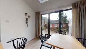 A dining area with a table and chairs, a sliding glass door leading to a garden, and two potted plants on the wall.