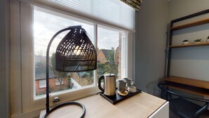 Una habitación con un ventanal grande, una lámpara colgante negra, un escritorio de madera, un hervidor y una bandeja con dos tazas.